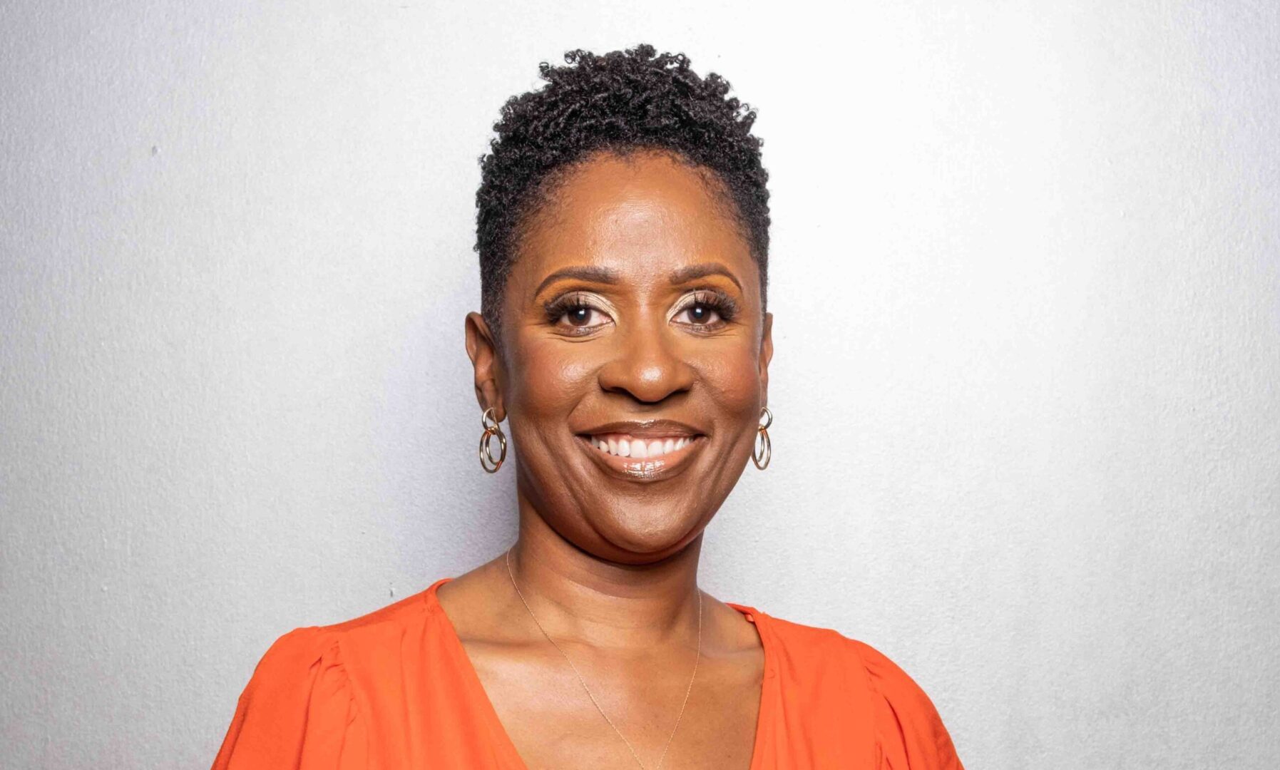 A woman in an orange shirt smiling for the camera.